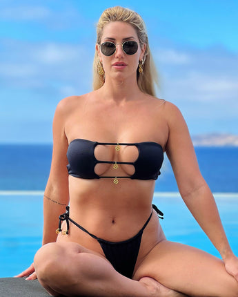 Embrace elegance with Naomi Besson's Isabella Brazilian bikini bottom. This luxurious black piece, adorned with gold logo charms, offers both Brazilian and thong coverage. Adjustable ties and high-quality double lycra fabric ensure a perfect, comfortable fit.
